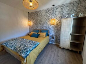 Quarto com cama, duas luminárias na parede, um guarda-roupa e papel de parede com padrão floral.