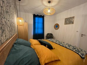 Ein Schlafzimmer mit einem Bett, zwei Hängeleuchten, einem fenster mit Vorhängen, einer Tür und einer Wand mit einem gerahmten Bild.