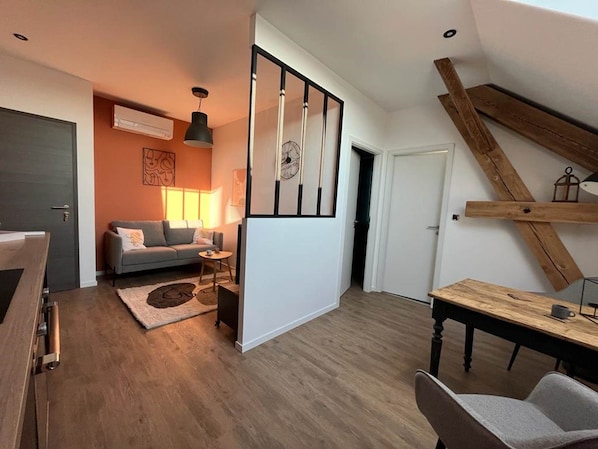 A modern living space with a sofa, a coffee table, and a dining table. There is a staircase with a wooden railing and a ceiling fan. - L'Orée des Sapins: 2-person vacation rental with spa access (AUBURE)