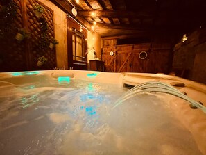 A hot tub with water jets, surrounded by wooden walls and a rustic interior. - L'Orée des Sapins: 2-person vacation rental with spa access (AUBURE)