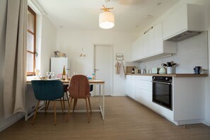 A modern kitchen with white cabinets, a dining area with a table and chairs, and a hanging light fixture. - A Mountain Getaway: Cabin for 2–4 People with Spa Access (AUBURE)