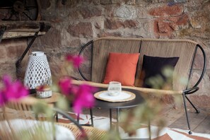 A wicker sofa with cushions against a brick wall, a white lantern, and a glass on a woven mat. - A Mountain Getaway: Cabin for 2–4 People with Spa Access (AUBURE)