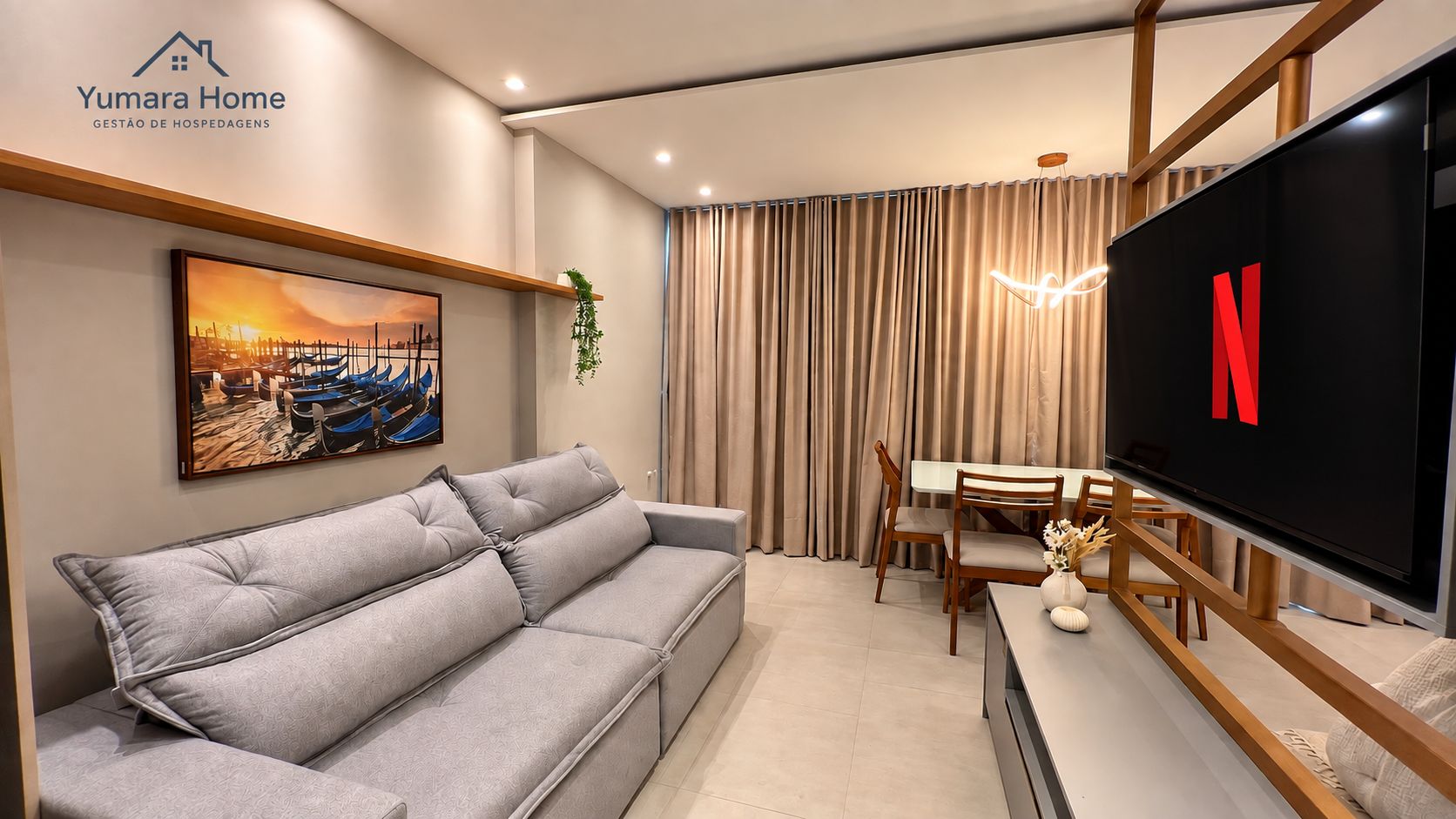 Una sala moderna con un sofá gris, una mesa de comedor con sillas, un televisor de pantalla plana y un cuadro en la pared.