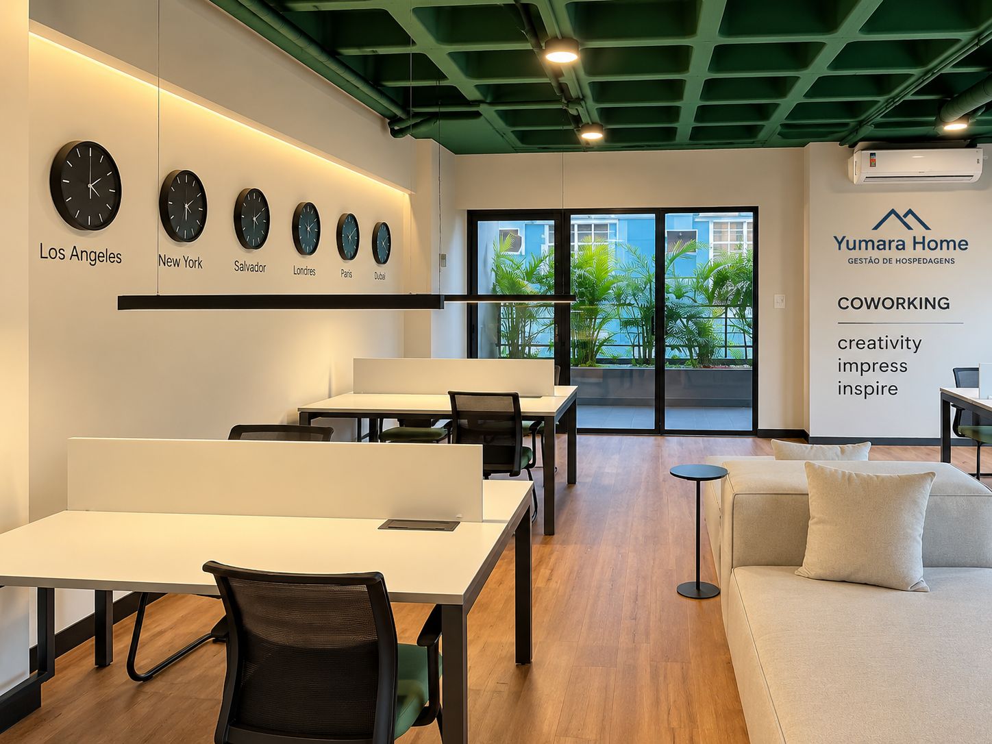 Espaço de trabalho moderno com mesas, cadeiras e um sofá. Há relógios indicando diferentes cidades e uma parede com a marca 'Yumara Home'.