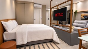 Quarto moderno com cama, televisão e sofá.