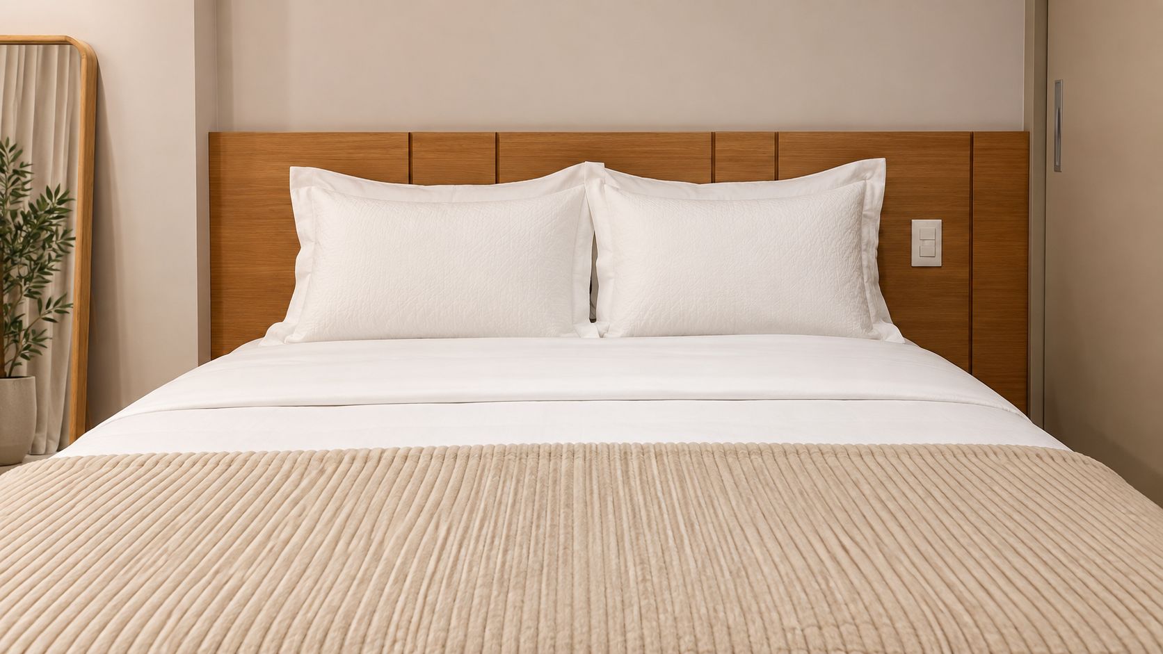 Cama com cabeceira de madeira, roupa de cama branca e manta bege texturizada.