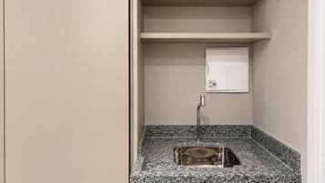 A small bathroom with a granite countertop sink, a mirror, and a wall-mounted light switch.