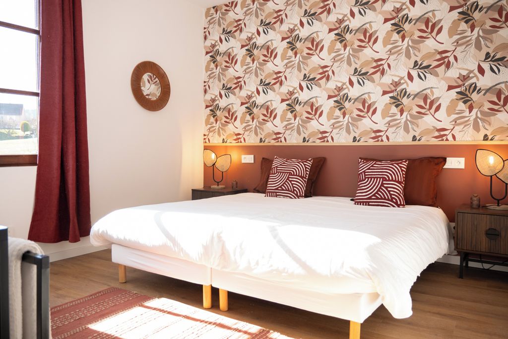 Ein Schlafzimmer mit einem großen Bett, einer Wand mit Muster, einem Nachttisch mit Lampen und einem Fenster mit Vorhängen.