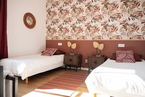 Ein Hotelzimmer mit zwei Einzelbetten, einem kleinen Nachttisch mit Lampe, einem Wandspiegel und einem Wandpapier mit Muster.