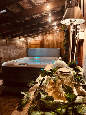 Ein Wellnessraum mit Whirlpool, Holzwänden, einer Decke mit sichtbaren Holzbalken und einem Tisch mit Pflanzen und einem Glasbehälter.