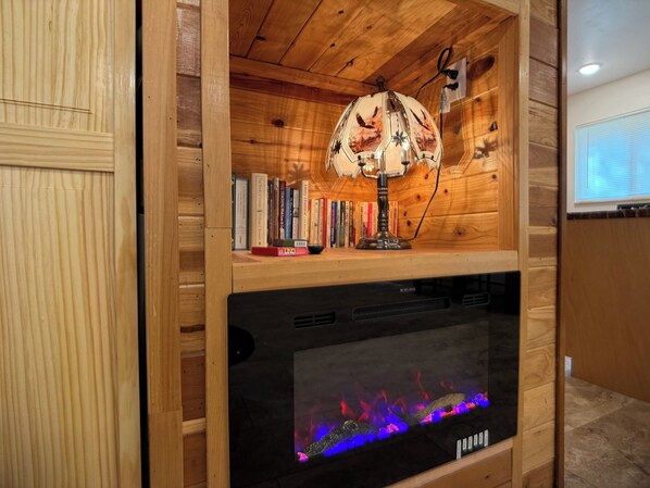 Una estantería de madera con libros, una lámpara decorativa y una chimenea con llamas de colores.