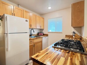 Una cocina con armarios de madera, un refrigerador blanco, un fregadero, una estufa y un ventanal con persianas.