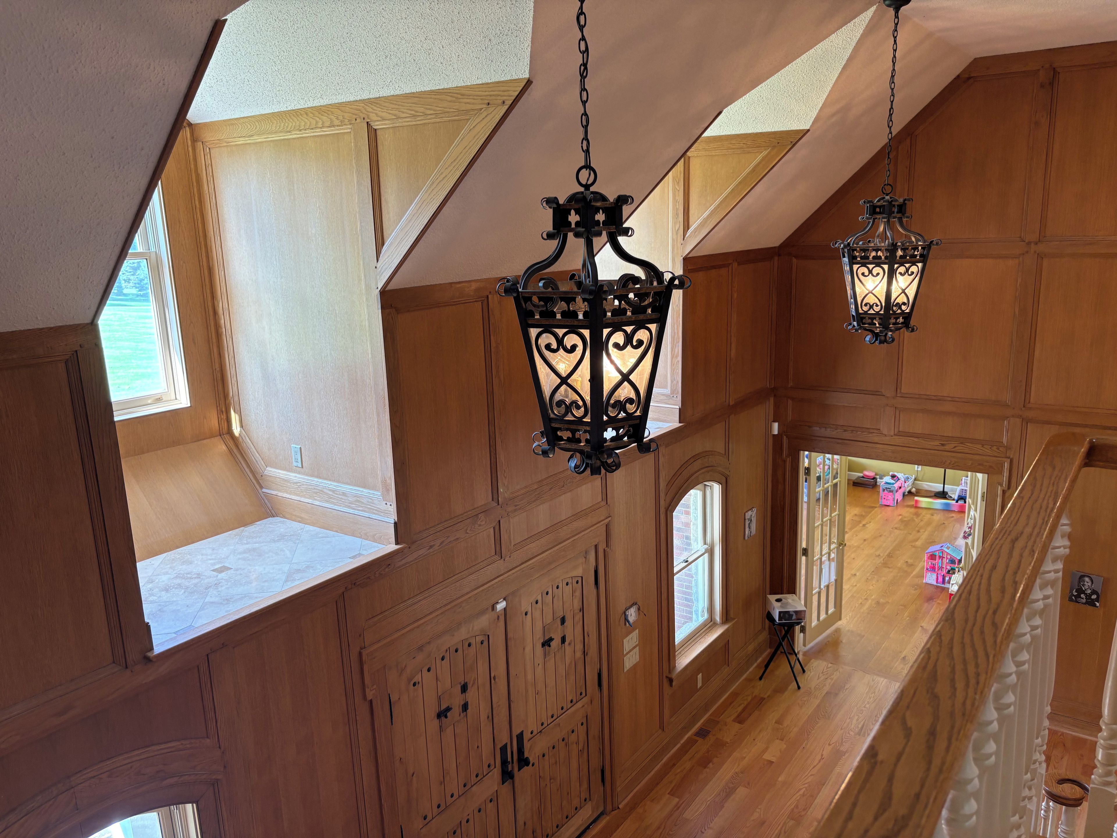A high-ceilinged room with wooden paneling, a sloped ceiling, and a view into another room.
