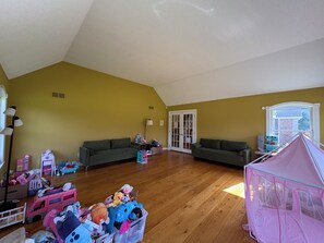 Ein geräumiges Wohnzimmer mit zwei Sofas, einem Spielbereich mit Spielzeug und einem großen Fenster.