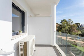 A balcony with a white radiator, a window with a closed blind, and a view of a green landscape with trees and a hill. - Sunset Med Hills 2BR Fuengirola (Fuengirola)