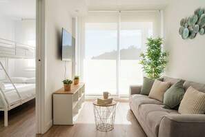 A modern living room with a sofa, a coffee table, and a TV. There is a balcony with a view of the hills. - Sunset Med Hills 2BR Fuengirola (Fuengirola)