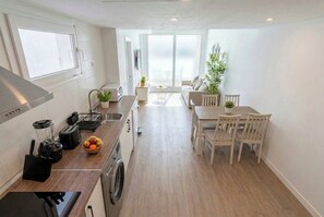 A modern kitchen with a dining area, a washing machine, and a large window providing natural light. - Sunset Med Hills 2BR Fuengirola (Fuengirola)