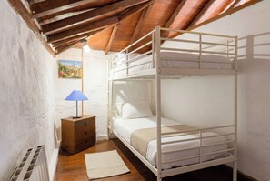 Un lit superposé avec une table de chevet en bois et une lampe, un mur blanc orné d’un tableau, et un plancher en bois.