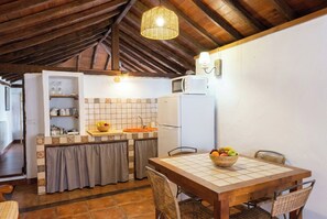 A compact kitchen with a dining area, featuring a tiled backsplash, a refrigerator, a microwave, and a hanging light fixture. - Las Ninfas Natural Escape 4 (Icod de los Vinos)
