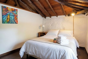 A bedroom with a wooden ceiling, a bed with white linens, a small potted plant, and a painting on the wall. - Las Ninfas Natural Escape 4 (Icod de los Vinos)