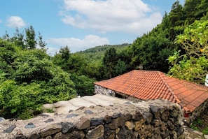 A stone wall with a red-tiled roof, surrounded by lush greenery and trees. - Las Ninfas Natural Escape 4 (Icod de los Vinos)