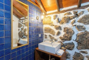 Une salle de bain avec un mur en pierre, un mur recouvert de carreaux bleus et un plafond en bois.