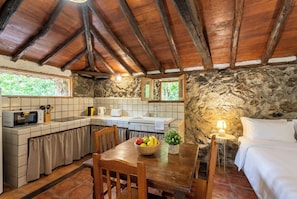 A rustic kitchen with a stone wall, wooden beams, a dining table with chairs, a microwave, and a sink. - Las Ninfas Natural Escape 3 (Icod de los Vinos)