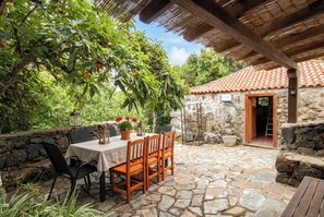 An outdoor patio with stone flooring, wooden furniture, and a stone wall. - Las Ninfas Natural Escape 2 (Icod de los Vinos)