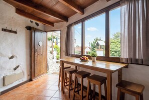 A wooden dining table with four stools, a window with curtains, and a door with a flower decoration. - Las Ninfas Natural Escape 2 (Icod de los Vinos)
