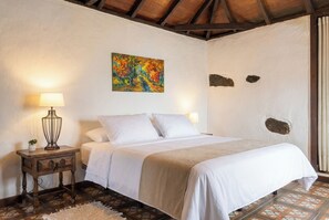 Ein Schlafzimmer mit einem Bett, zwei Nachttischlampen, einem Gemälde und einer rustikalen Decke.