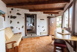 Ein rustikaler Raum mit Holzboden, einem Bett mit kariertem Überwurf, einem Holztisch mit Topfpflanze und einem Fenster mit Vorhängen.