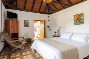 A bedroom with a bed, a wooden chair, a television, and artwork on the walls. - Las Ninfas Natural Escape 2 (Icod de los Vinos)