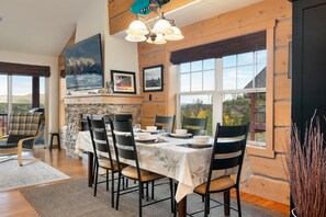 Un comedor con una mesa dispuesta para cuatro, paredes de madera, una chimenea de piedra y un ventanal con vistas al exterior.