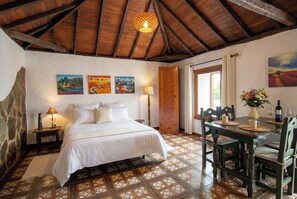 A bedroom with a bed, a table with chairs, and a door. - Las Ninfas Natural Escape 1 (Icod de los Vinos)