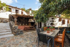 A stone patio with a table and chairs, a stone wall, and a building with a tiled roof. - Las Ninfas Natural Escape 1 (Icod de los Vinos)