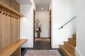 Ein modernes Interieur mit Holzböden, einer Treppe und einem Flur, der zu einem Raum mit Spiegel und Vase führt.