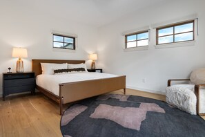 Ein Schlafzimmer mit einem Bett, zwei Nachttischen, einem Sessel, einem Teppich und zwei Fenstern.