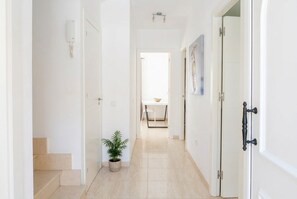 A hallway with a potted plant, a white door with a black handle, and a white wall with a light switch. - Corralejo 3BR House with Pool (Corralejo)
