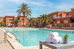 A swimming pool with a lifeguard stand, a table with rolled towels, and palm trees. - Corralejo 3BR House with Pool (Corralejo)
