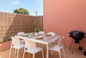 A patio with a table set for six, surrounded by white chairs, a small potted plant, and a barbecue grill. - Corralejo 3BR House with Pool (Corralejo)