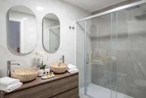 Une salle de bain moderne avec deux vasques rondes en marbre, une douche en verre et un meuble-lavabo en bois.