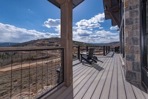 Eine Holzterrasse mit Blick auf eine gebirgige Landschaft, einer Steinmauer und einem Metallgeländer.