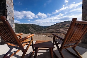 Zwei Holzstühle und ein kleiner Tisch auf einem Balkon mit Blick auf eine Berglandschaft.