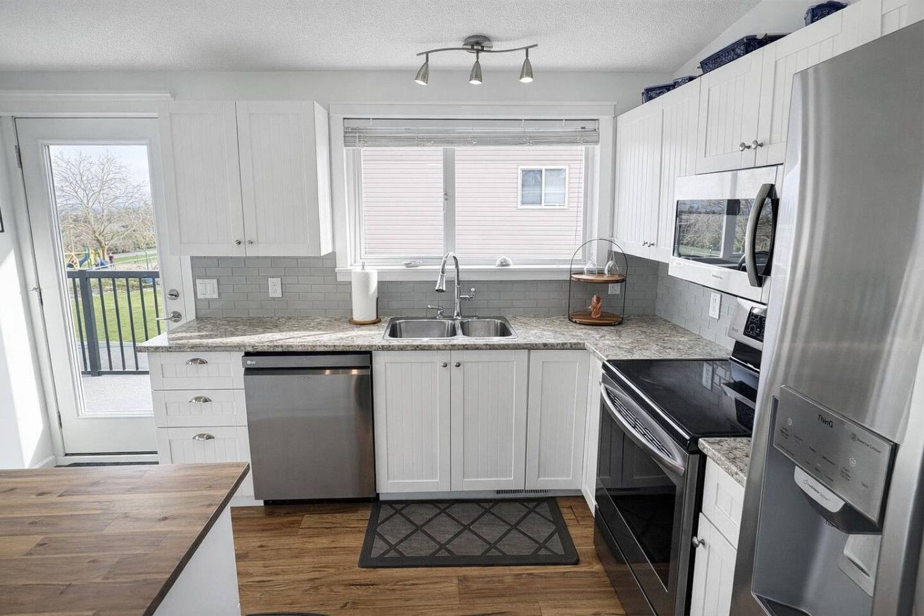 A modern kitchen with white cabinetry, a built-in dishwasher, a double sink, a microwave, and a stove.