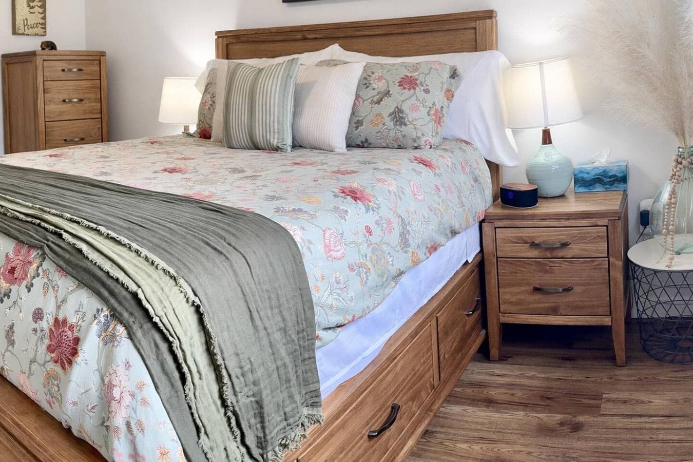 A bedroom with a bed, two bedside tables, a nightstand, a lamp, and a wall-mounted shelf.