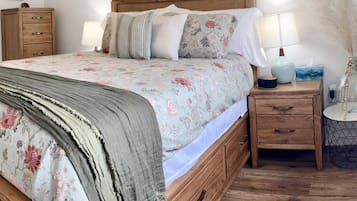 A bedroom with a bed, two bedside tables, a nightstand, a lamp, and a wall-mounted shelf.