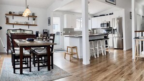A modern kitchen with white cabinets, stainless steel appliances, and a wooden dining table with chairs. - Seaview Suite · sunrise deck, BBQ, firepit & 3-bed (Campbell River)