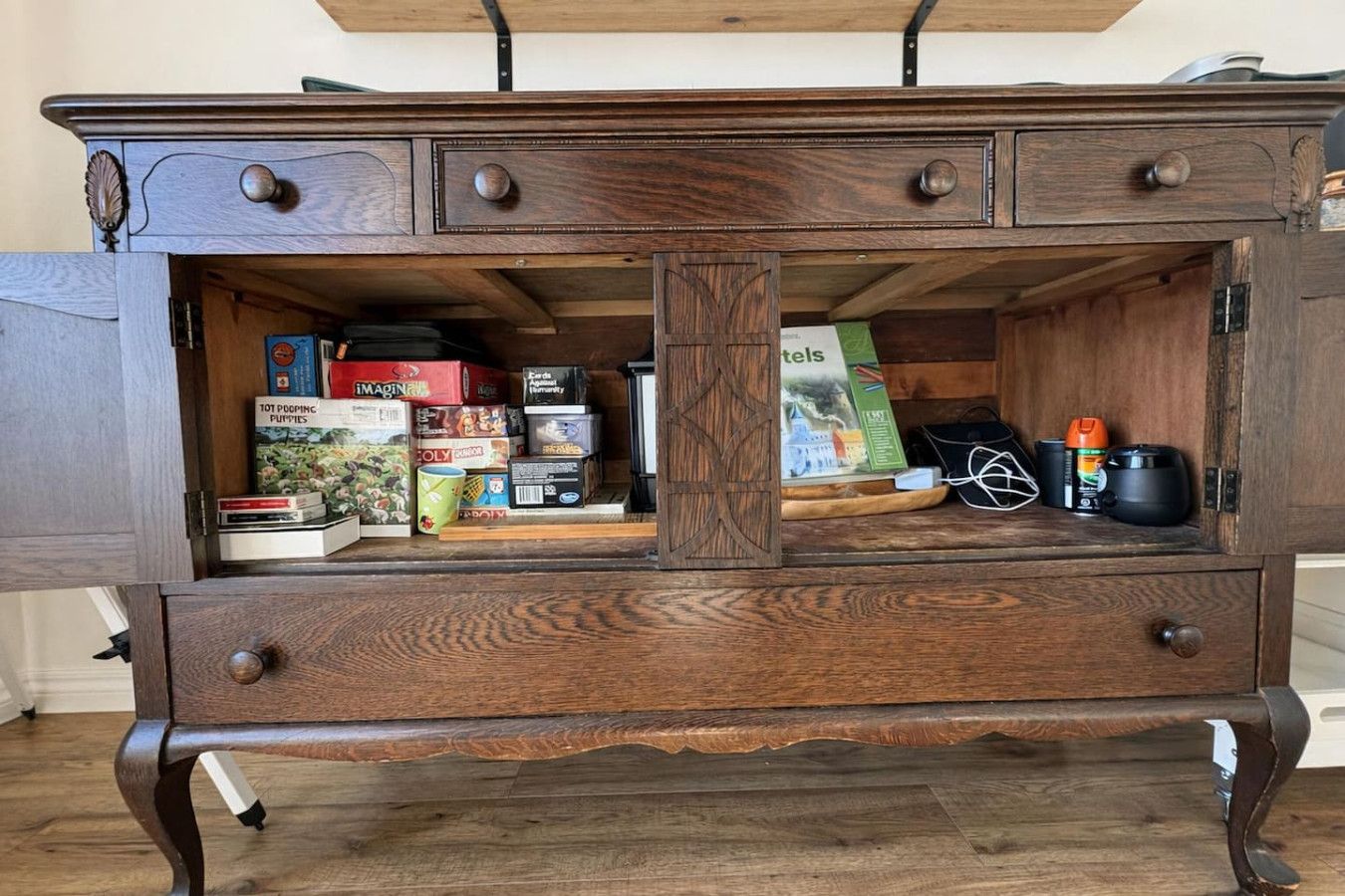 Un meuble en bois doté de nombreux tiroirs et d’étagères, contenant divers objets tels que des livres, des boîtes et un petit appareil électronique.