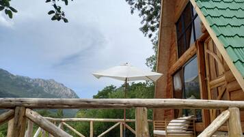 A wooden deck with a view of mountains, a white umbrella, and a wooden chair.