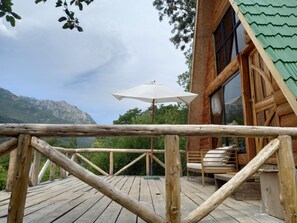A wooden deck with a view of mountains, a white umbrella, and a wooden chair.